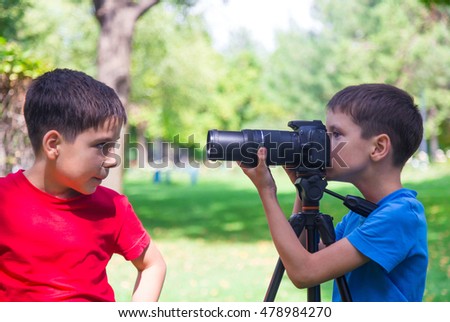 Two young boys take pictures of each other using a digital camera outdoors. Sunny summer day in a park