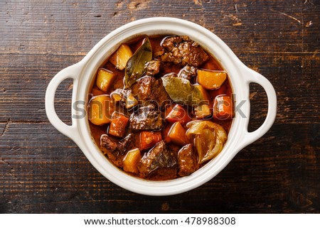 Beef meat stewed with potatoes, carrots and spices in ceramic pot on wooden background Royalty-Free Stock Photo #478988308