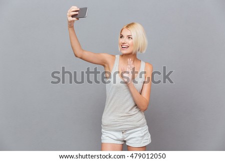 Cheerful lovely young woman taking selfie using mobile phone over gray background