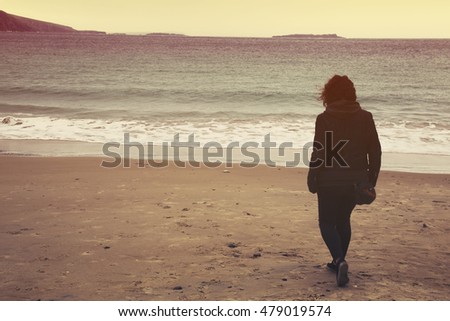 Women on beach walks towards calm ocean at sunset