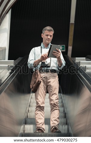 Confident man on the escalator, he is using a digital tablet and searching for directions