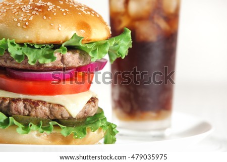 Big juicy traditional American burger with grilled meat and slices fresh vegetables closeup on a white plate on a wooden table. Food and beverages. Selective focus with shallow depth of field