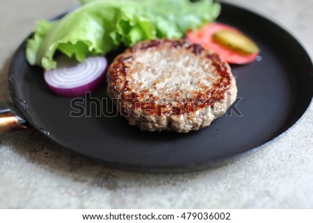 Vintage pan with fried juicy cutlet burger with slices of tomato and lettuce. Food and Cooking. Selective focus with shallow depth of field.