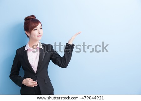 business woman smiles and shows something to you isolated on blue background, asian