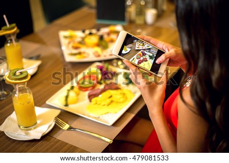 Elegant woman taking photos of food in restaurant with her smartphone during dinner. Toned image.
