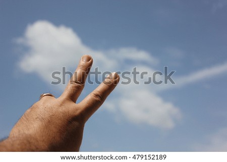 two fingers pointing to  the white cloud on blue sky