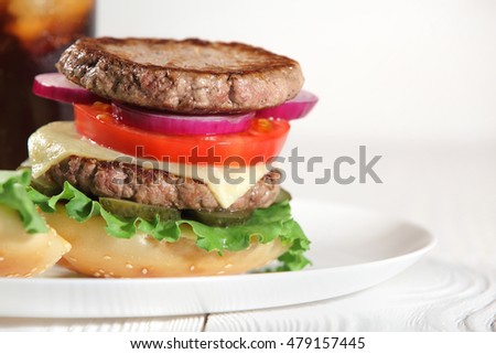 Big juicy traditional American burger with grilled meat and slices fresh vegetables closeup on a white plate on a wooden table. Food and beverages. Selective focus with shallow depth of field