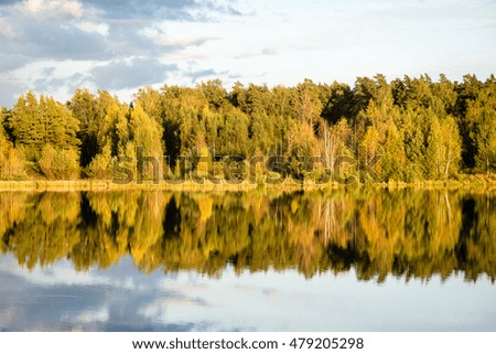 Beautiful autumn sunset at the lake with blue sky, red and orange clouds, green trees and water with reflection
