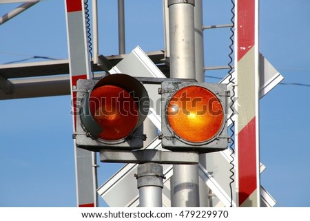 Orange Flashing Railroad Crossing Lights Up Close with Right Light Illuminated, Orange and White Striped Guard Arms Up, in Afternoon Sun with Blue Sky Behind