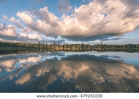 Beautiful summer sunset at the lake with blue sky, red and orange clouds, green trees and water with reflection - vintage film look