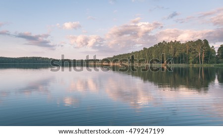 Beautiful summer sunset at the river with blue sky, red and orange clouds, green trees and water with reflection - vintage film look