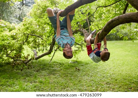 friendship, childhood, leisure and people concept - two happy kids or friends hanging upside down on tree and having fun in summer park Royalty-Free Stock Photo #479263099