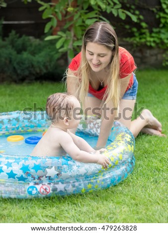 Cute baby boy playing in swimming pool at backyard with young mother