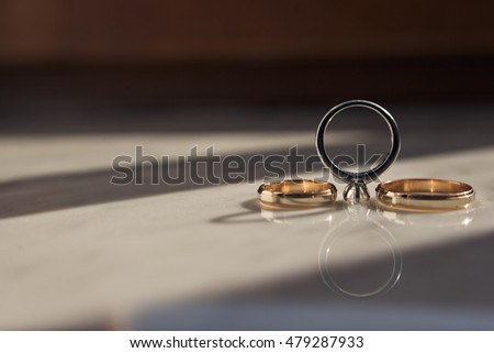 Golden wedding rings and silver engagement ring lie on white table