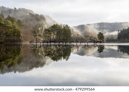 Morning mist reflection over the lake with little house and forest in the background