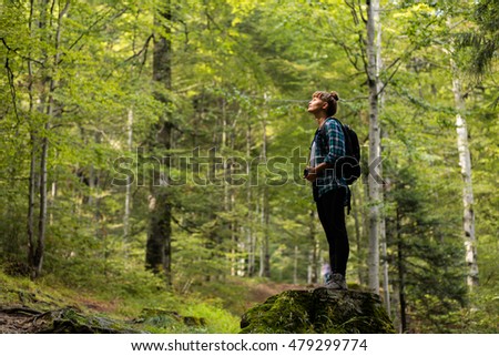 single traveler woman sitting on a log with her backpack and camera in the middle of a forest watching and enjoying the nature