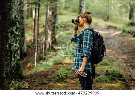 young woman with plaid male shirt traveling alone with her backpack and camera, taking picture of the nature