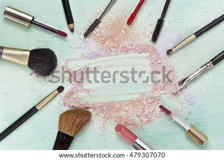 Makeup brushes and lipstick on teal blue background, with traces of powder and blush, forming a frame; horizontal template for makeup artist's business card or flyer design; with copyspace