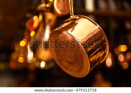 Copper kitchenware (pots, pans, jugs) hang from the ceiling in the kitchen. Royalty-Free Stock Photo #479313718