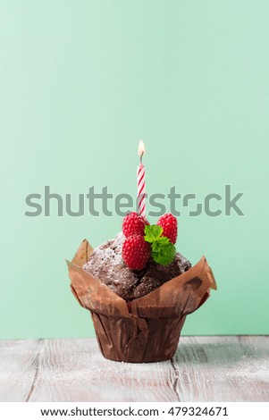 Delicious birthday chocolate muffin with fresh raspberries and candle on a green mint background, selective focus. Toned image with copy space