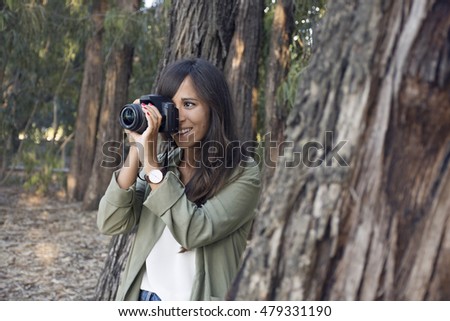 Close up of a young beautiful woman with an reflex camera shooting to you in autumn