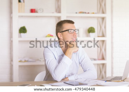 Portrait of smiling young businessman sitting at table in modern office interior