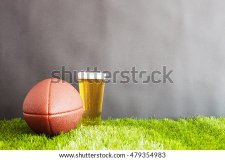 Football and beer glass on grass and black background