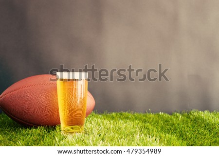 Football and beer glass on grass and black background