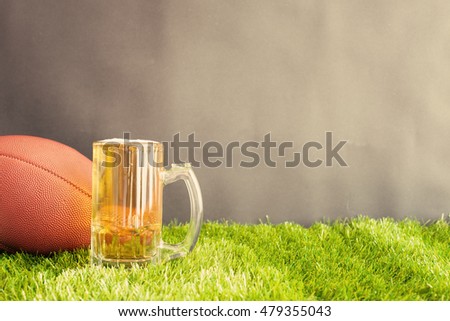 Football and beer jar on grass and black background 