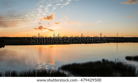 Beautiful summer sunset at the river with blue sky, red and orange clouds, green trees and water with reflection