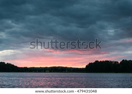 Dramatic summer sunset at the river with blue sky, red and orange clouds, green trees and water with reflection