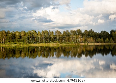 Beautiful summer sunset at the lake with blue sky, red and orange clouds, green trees and water with reflection