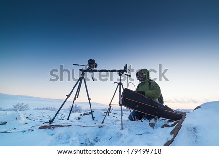 Man with photo camera on tripod taking timelapse photos in the arctic tundra. Poor lighting conditions.
