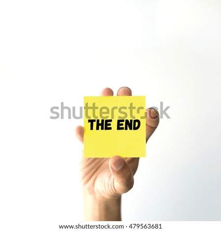Hand holding yellow sticky note written THE END 