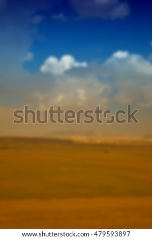Golden field under blue sky blur background. Defocused image, blur of photo spring summer landscape with sun. Beautiful field of green grass and sky. Background bright  with cloudy sky and grass.