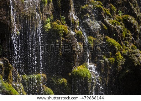 
Jets waterfall flowing on rocks overgrown with green grass .