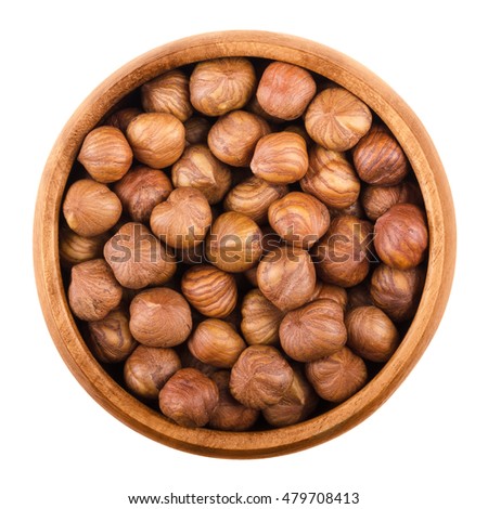 Hazelnuts in a wooden bowl on white background. Shelled ripe seeds of a cultivated Corylus species. Edible raw fruits. Isolated macro food photo close up from above.