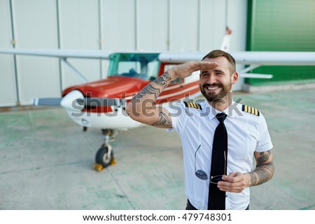 Smiling handsome young white man pilot posing at the hangar with private motor airplane. 