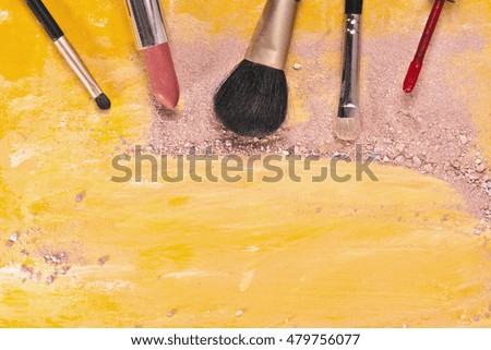 Makeup brushes and lipstick on a vibrant golden yellow background, with traces of powder and blush on it; a horizontal template for a makeup artist's business card or flyer design; with copyspace