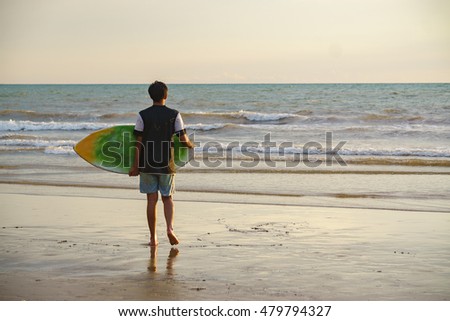 Unrecognizable young asian man from behind stands with skimboard on the shore of Tanjung Aru beach Sabah Malaysia.
