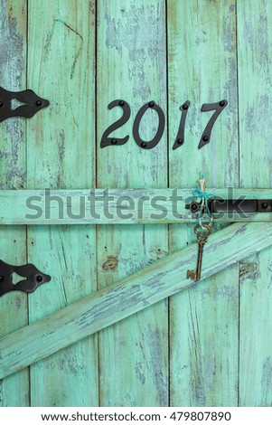 Year 2017 in black iron numbers and brass skeleton key hanging on antique rustic mint green wooden door; Happy New Year concept