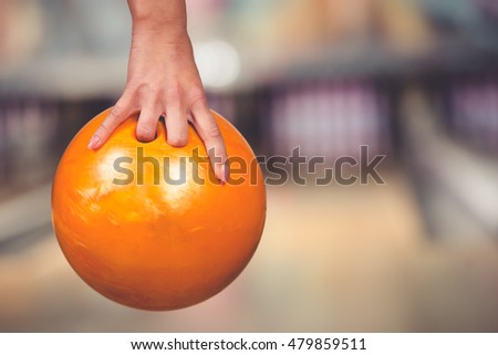 Close-up hand of woman is holding ball against bowling alley.
