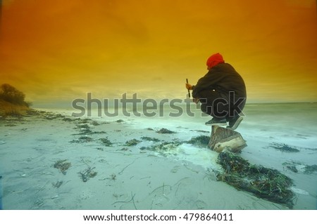 Young man sitting on a stone at a Beautiful orange sunset on the beach