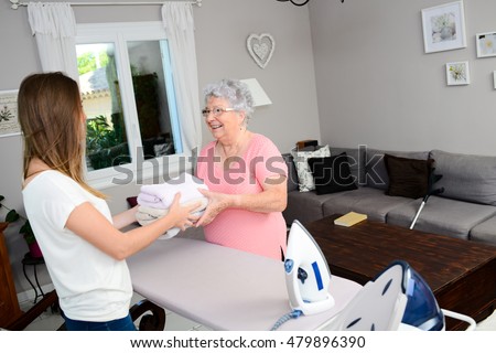 cheerful young girl ironing and helping with household chores an elderly woman at home  Royalty-Free Stock Photo #479896390
