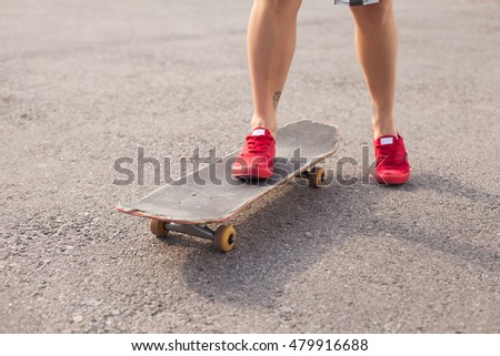 The woman with tattoo  in pink shoes is skating on an old skate on the background of asphalt.