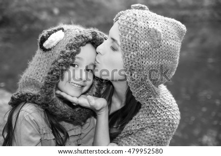 Mother with daughter both wearing hoodies and warm clothing sitting outdoors embracing happily, green nature background, black white edition