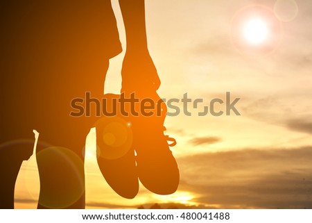 Silhouette boy holding canvas shoes on sunset