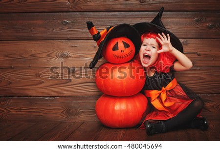 funny child girl in witch costume for Halloween with pumpkin Jack on a dark wooden background