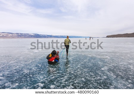 Girl with a sledge and trekking pole is on the blue ice of Baikal