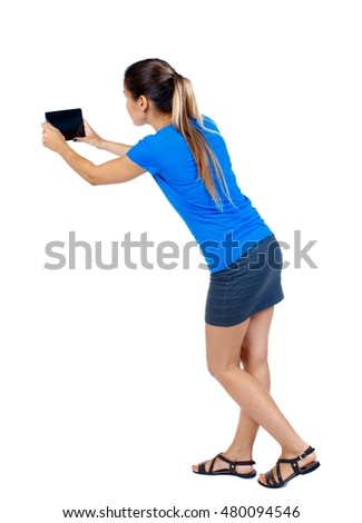 back view of standing young beautiful woman using a mobile phone. Isolated over white background. girl in a short skirt and a blue T-shirt photographed on the plate.